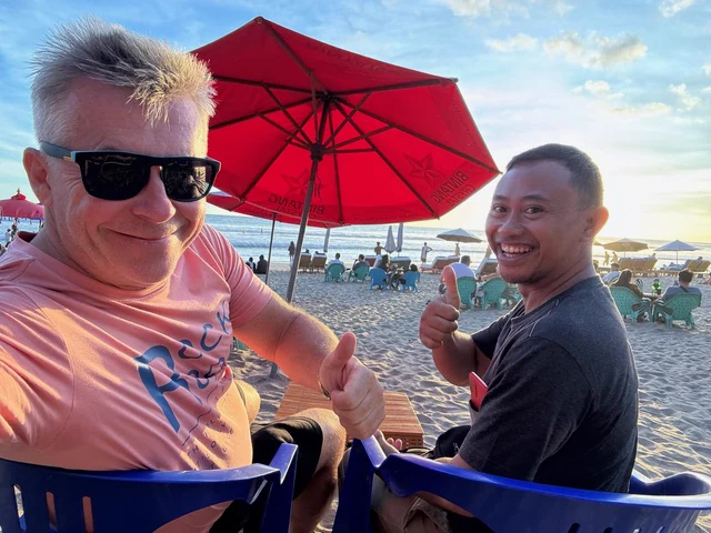 Two people sitting together beneath a red beach parasol