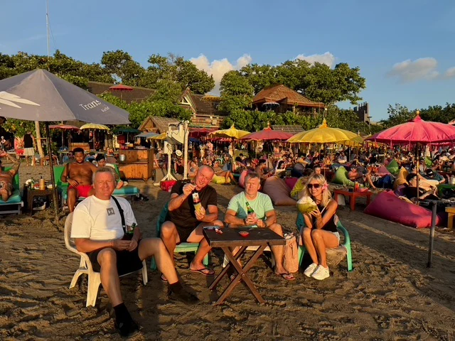 A group seated together on a beach beneath colourful parasols