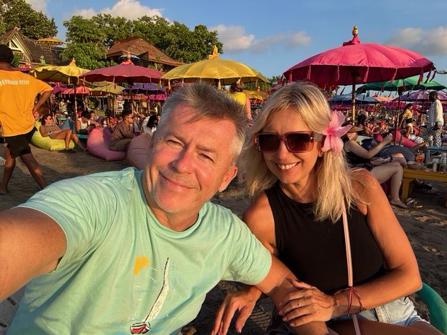 Two travellers smiling at a beach gathering in the late afternoon