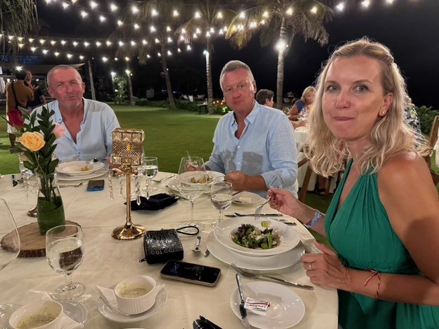 Travellers at an outdoor dinner table beneath strings of lights
