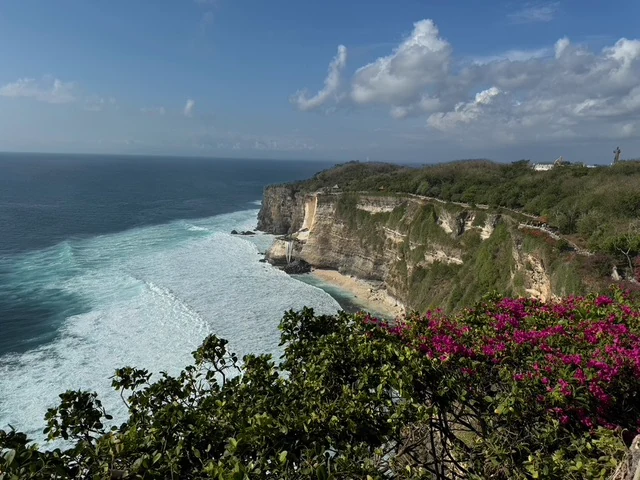 Waves breaking along a sandy beach beneath high coastal cliffs