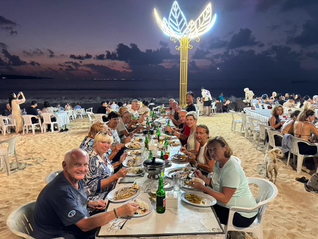 A group dining at a long table on the beach at dusk