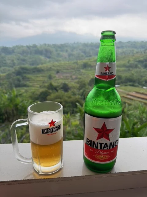 A bottle and glass on a ledge overlooking a green tropical landscape